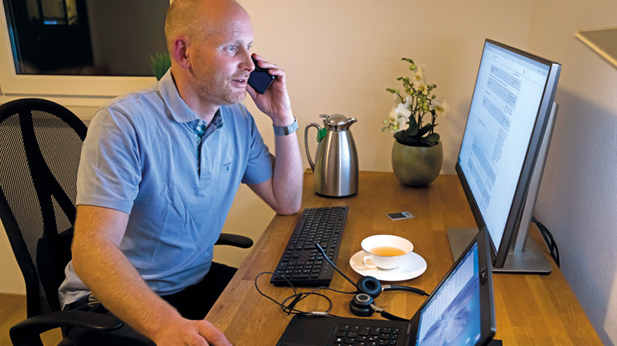 Arbeitnehmer sitzt am heimischen Arbeitsplatz und telefoniert.