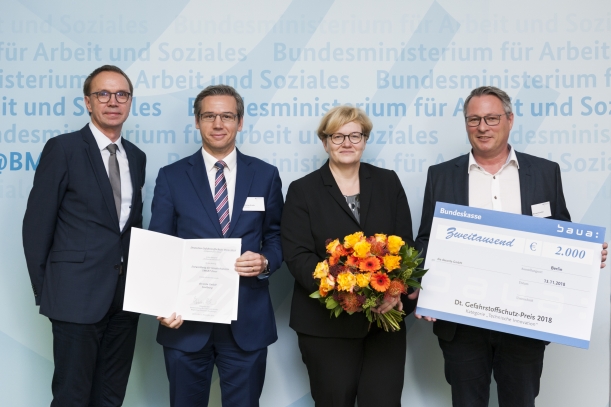 Rüdiger Pipke (Bundesanstalt für Arbeitsschutz und Arbeitsmedizin), Christian Krolle (deconta GmbH), Anette Kramme (BMAS) und Michael Scholten (deconta GmbH) präsentieren Gewinnerscheck und Urkunde