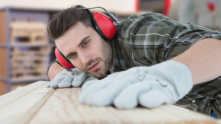 Worker with hearing protection inspects wooden board.